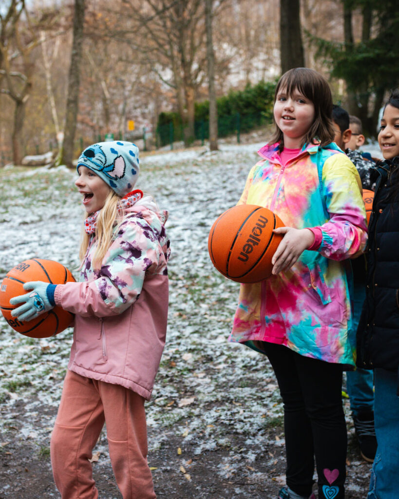 Lächelnde Kinder halten Basketbälle am Standort des neuen, von Lindner Bau installierten Basketballkorbes in Lugau. Fokus auf die positive Wirkung der Kooperation und der Spende.