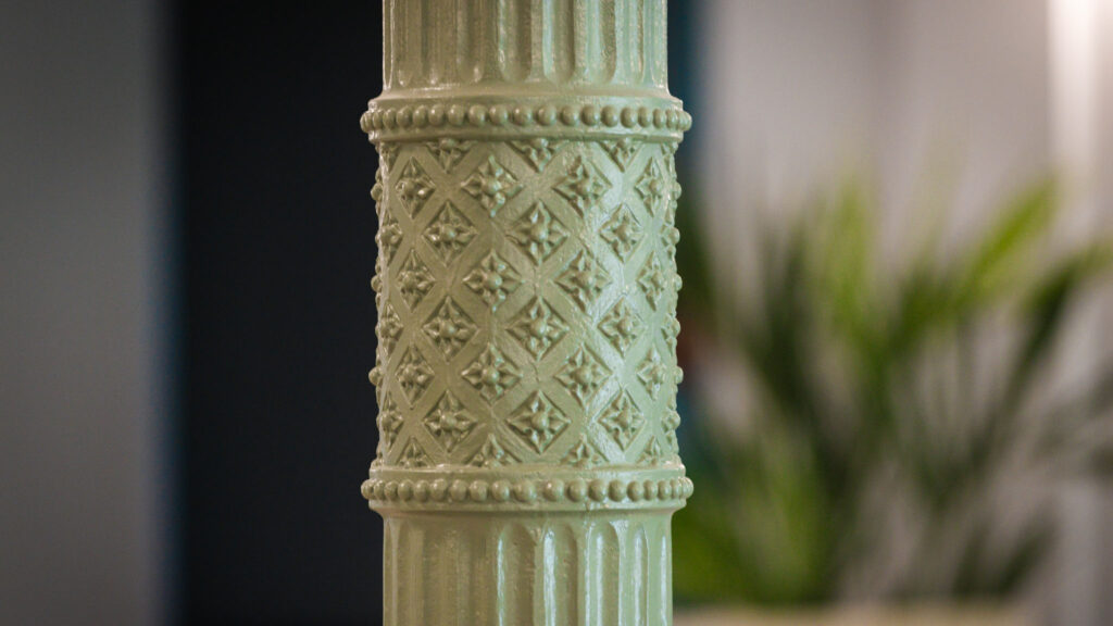 Nahaufnahme einer grünen, verzierten Säule mit detaillierten Mustern wie Perlenreihen und einem Rautenmuster mit Blumenmotiven.