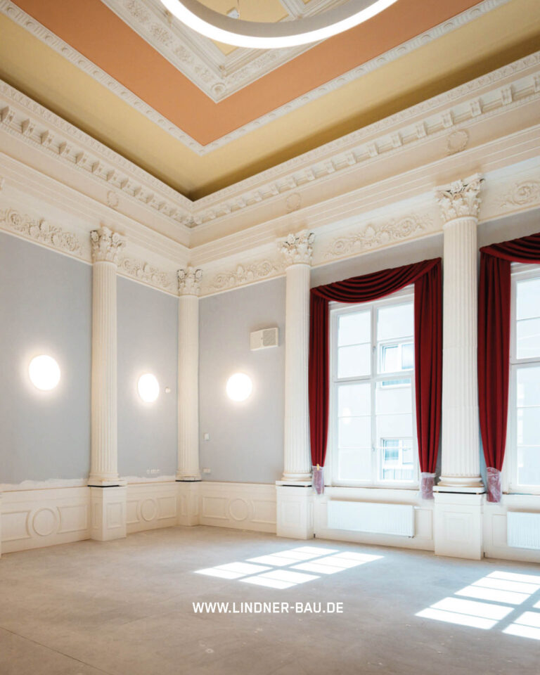 Gesamtansicht des klassisch gestalteten Festsaals mit hoher Decke, umlaufenden Säulen, runder Beleuchtung und großen Fenstern.