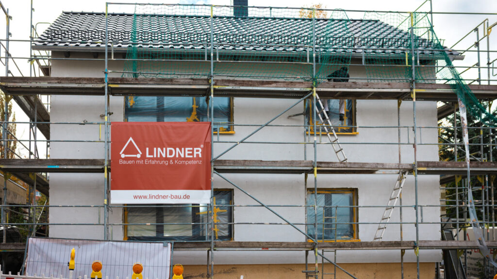 Eingerüstetes Einfamilienhaus mit Lindner-Bautafel während der Fassadensanierung.