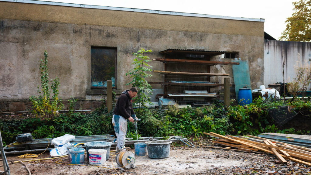 Bauarbeiter mischt Außenputz oder Mörtel mit einem Rührgerät in einem Eimer auf der Baustelle an.