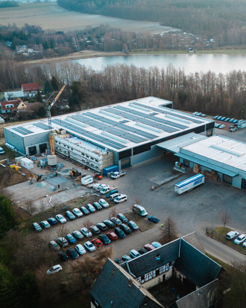 Draufsicht auf eine aktive Baustelle von Lindner Bau mit Turmdrehkran, Baggern und Containern für den Industriebau.