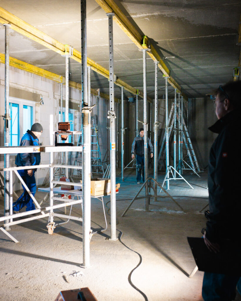 Arbeiter von Lindner Bau im Innenraum eines Rohbaus bei der Montage von Deckenstützen und Schalungsträgern.