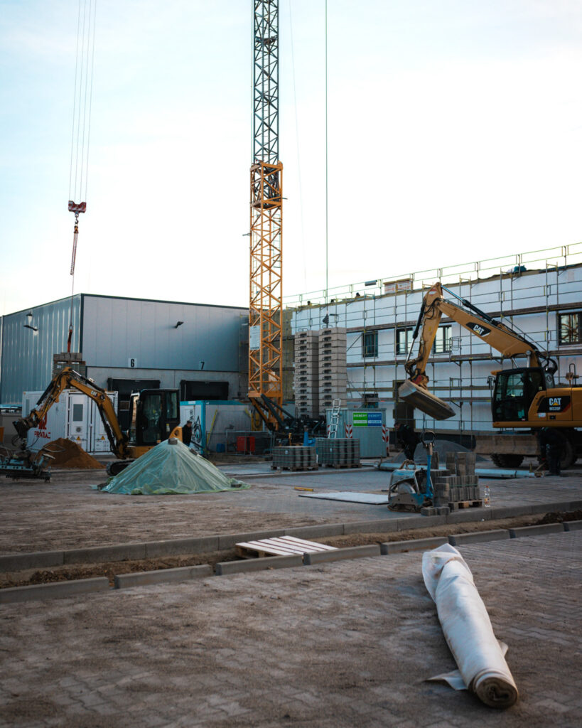 Außenanlage vor einem Neubau mit CAT-Bagger, Baustelleneinrichtung und Turmdrehkran von Lindner Bau.