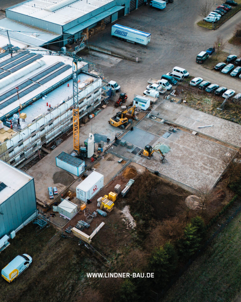Luftaufnahme einer organisierten Baustelle von Lindner Bau mit Kränen, Baggern und Containern für den Gewerbebau.