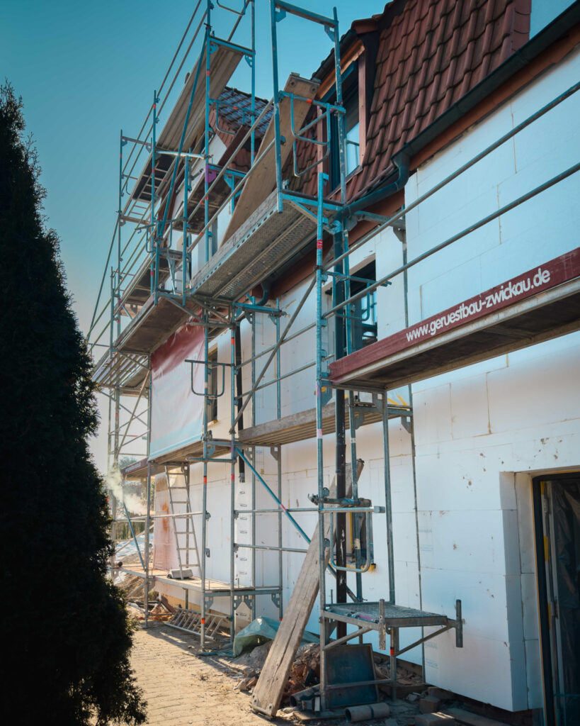 Seitenansicht eines Hauses mit weißer Fassadendämmung und professionellem Metallgerüst während der Bauphase.