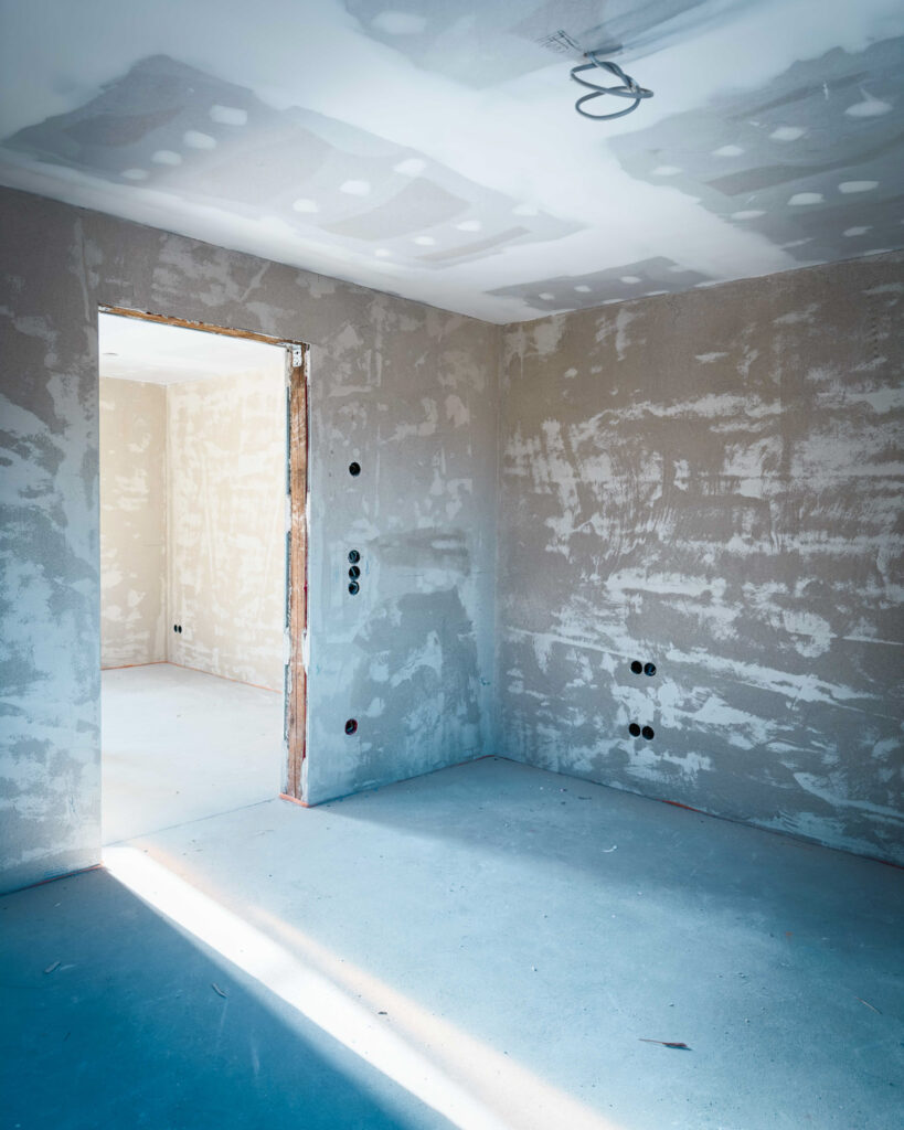 Rohbau-Innenraum mit frisch verputzten Wänden, Deckenspachtelung und Vorbereitungen für die Elektroinstallation.