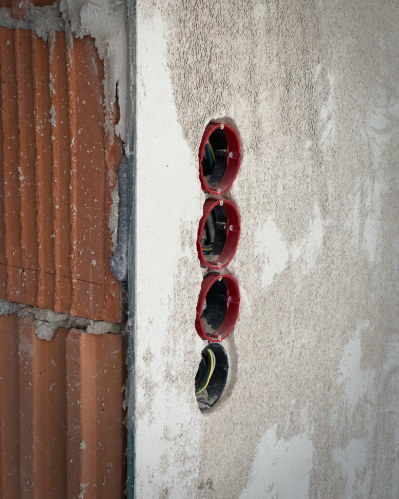 Detailaufnahme von vier installierten Unterputzdosen für Steckdosen in einer frisch verputzten Ziegelwand.