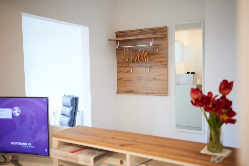 Objekteinrichtung in der Zahnarztpraxis: Stilvolle Holz-Garderobe und harmonisches Farbkonzept für einen schlüsselfertigen Praxis-Empfang.