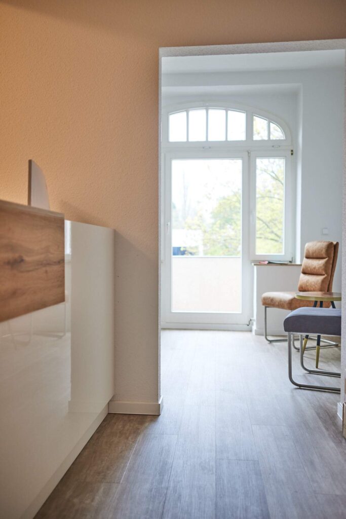 Einladendes Praxis-Design: Blick vom modernen Empfangstresen in Holzoptik in den hellen Wartebereich mit stilvollem Rundbogenfenster.