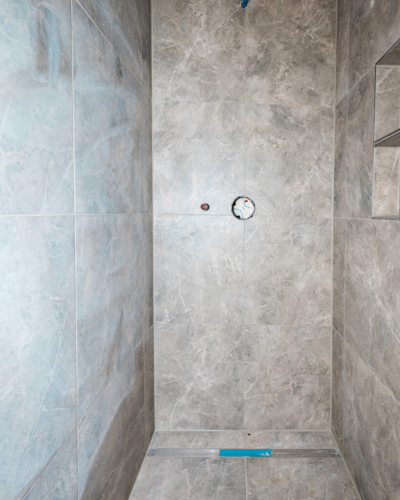 Detailaufnahme einer bodengleichen Dusche mit modernen, großformatigen Fliesen in Natursteinoptik.