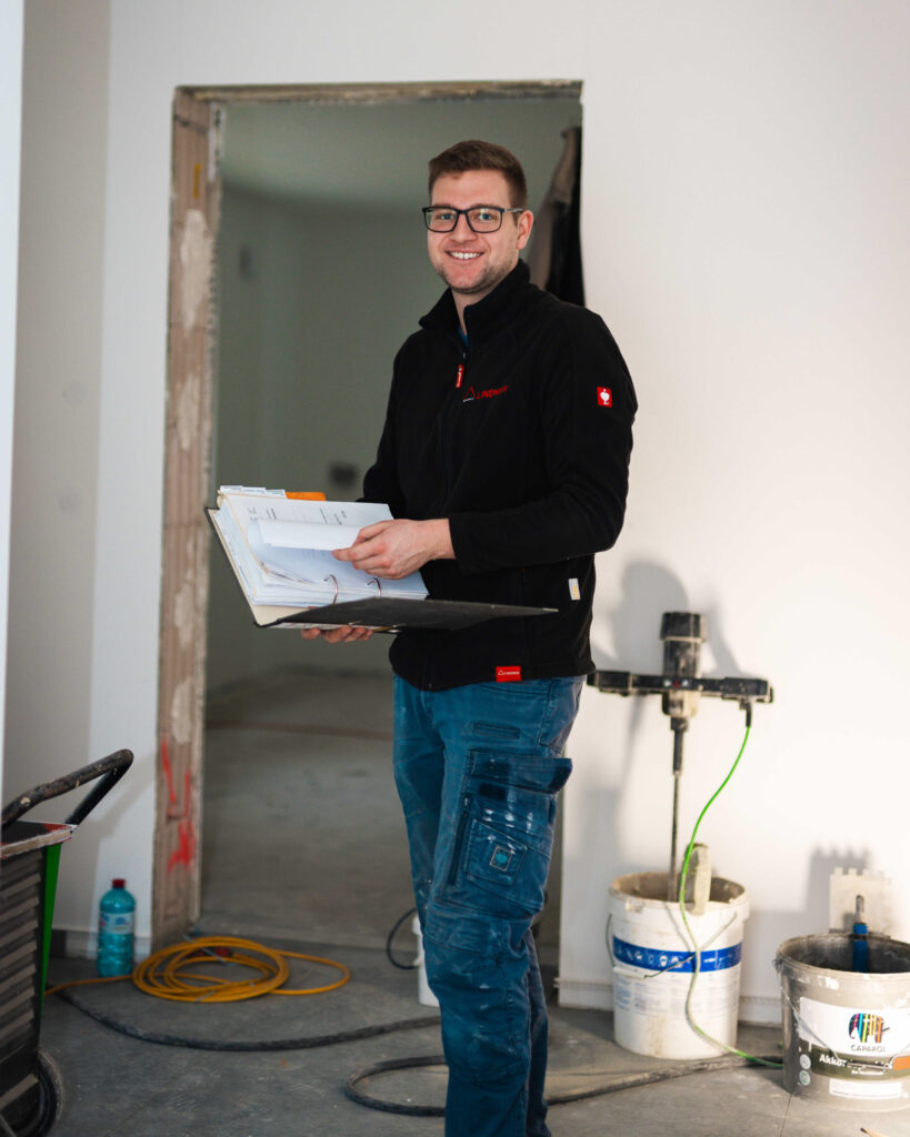 Handwerker von Lindner Bau mit Bauplänen in einem neu gestalteten Türdurchgang auf der Baustelle.