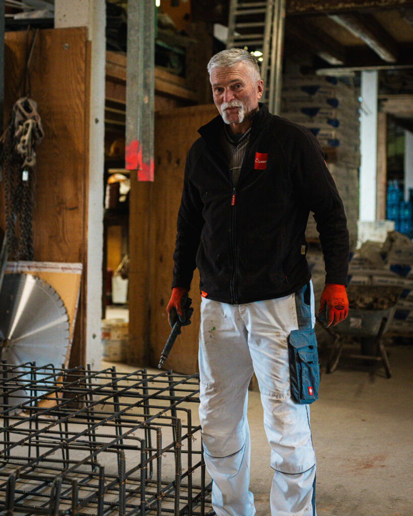 Erfahrener Bauhandwerker in Arbeitskleidung steht vor einer Bewehrungskonstruktion aus Stahl.