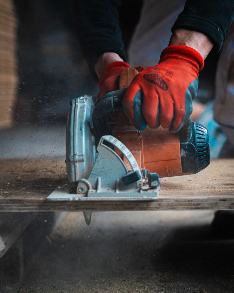 Nahaufnahme: Handwerker mit Schutzhandschuhen schneidet eine Holzplatte präzise mit einer Handkreissäge.