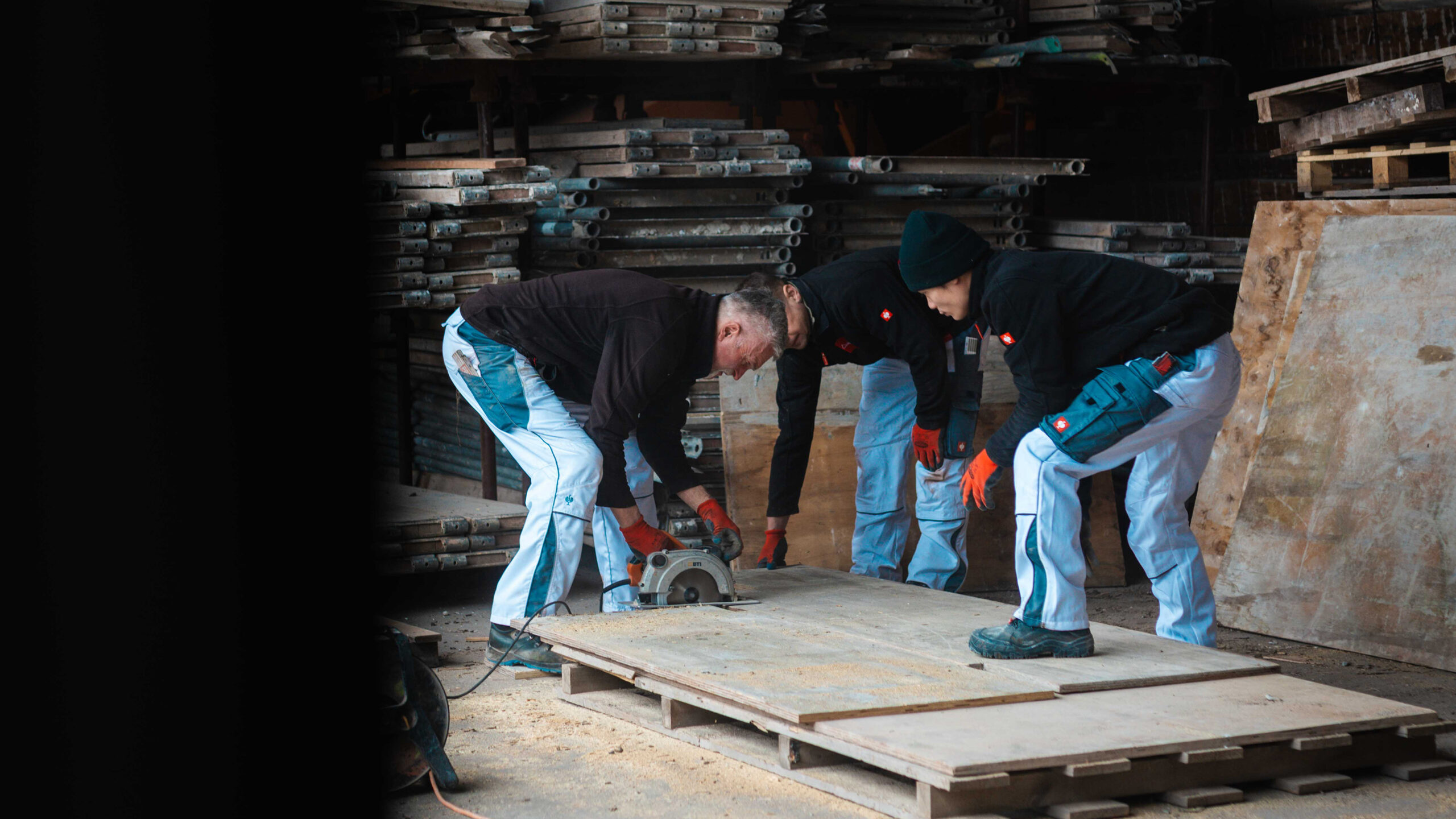 Teamarbeit auf dem Bau: Drei Handwerker beim Zuschneiden von Schalungsplatten mit der Kreissäge.