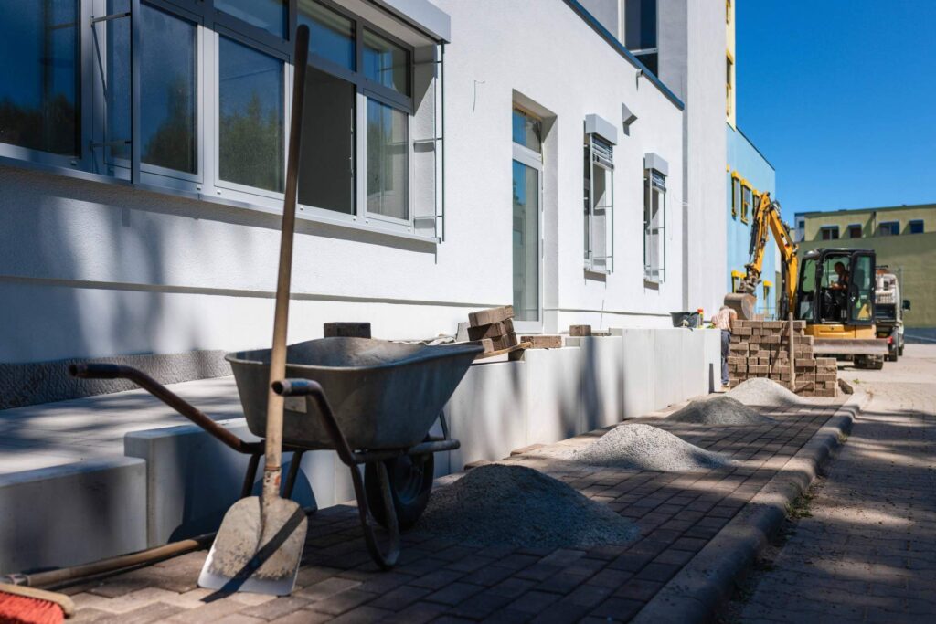 Garten- und Landschaftsbauarbeiten am Krankenhaus mit Schubkarre, Schaufel und Minibagger zur Fertigstellung der Außenanlagen.