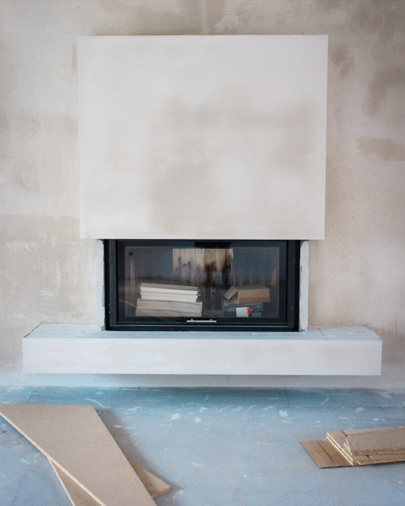 Moderner, minimalistischer Kamineinsatz im Rohbau-Stadium mit weißer Verkleidung während der Montage im Wohnbereich.