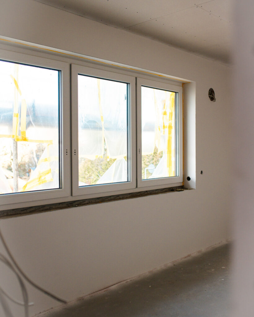 Dreiflügeliges weißes Kunststofffenster im Rohbau, abgeklebt mit Schutzfolie zum Schutz vor Putzarbeiten.