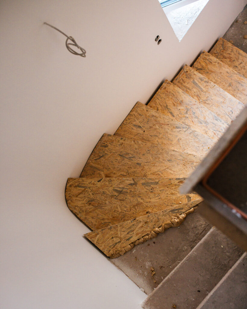 Draufsicht auf eine im Bau befindliche Treppe mit OSB-Platten-Stufen und sichtbarem Montageschaum an den Wandanschlüssen.