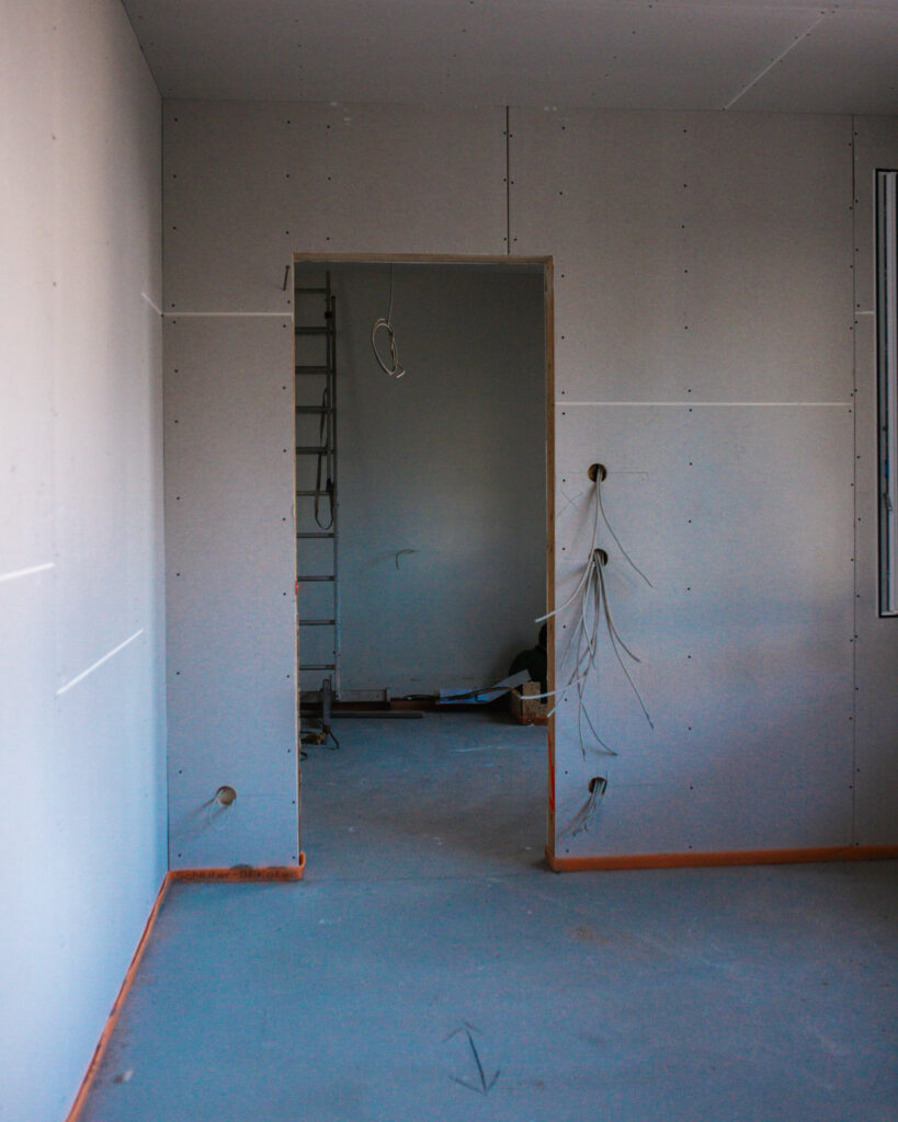 Rohbau-Innenansicht eines Raumes mit fertig gestellten Gipskartonwänden, Tür-Ausschnitt und Markierungen für Steckdosen.