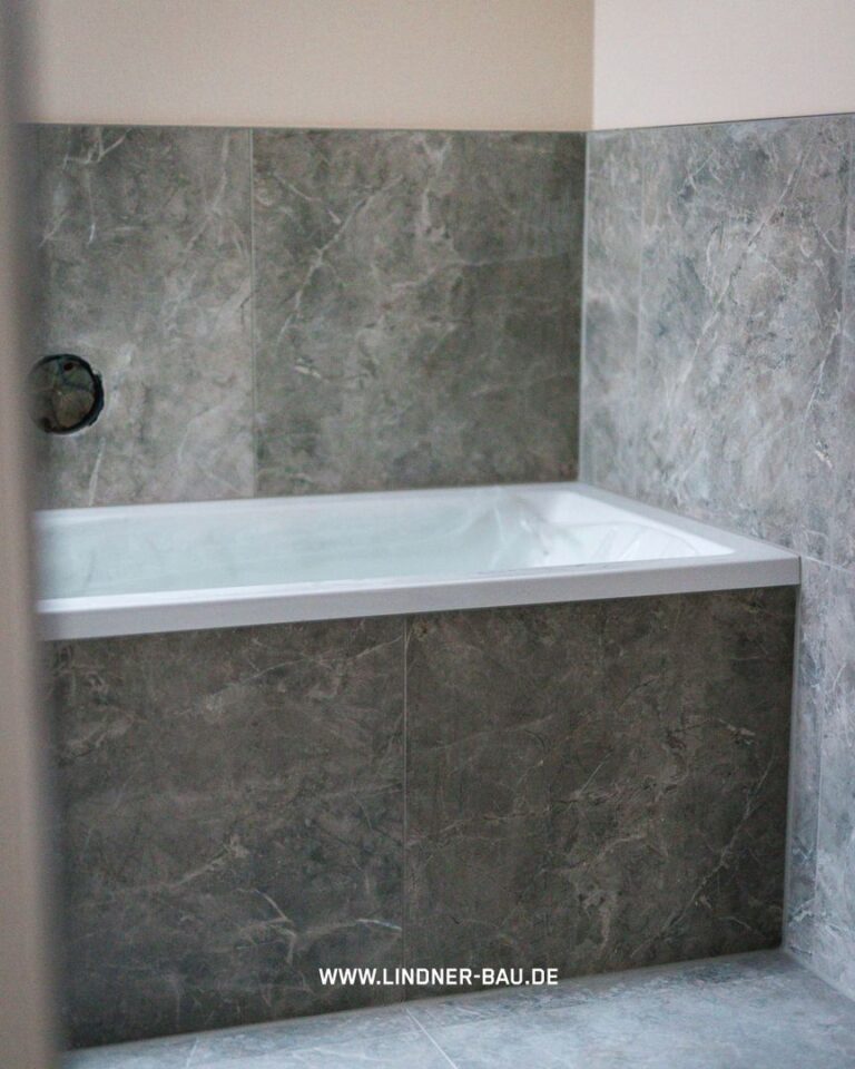 Modernes Badezimmer mit eingebauter weißer Badewanne und großformatigen Marmorfliesen in Grau-Anthrazit an Wand und Verkleidung.