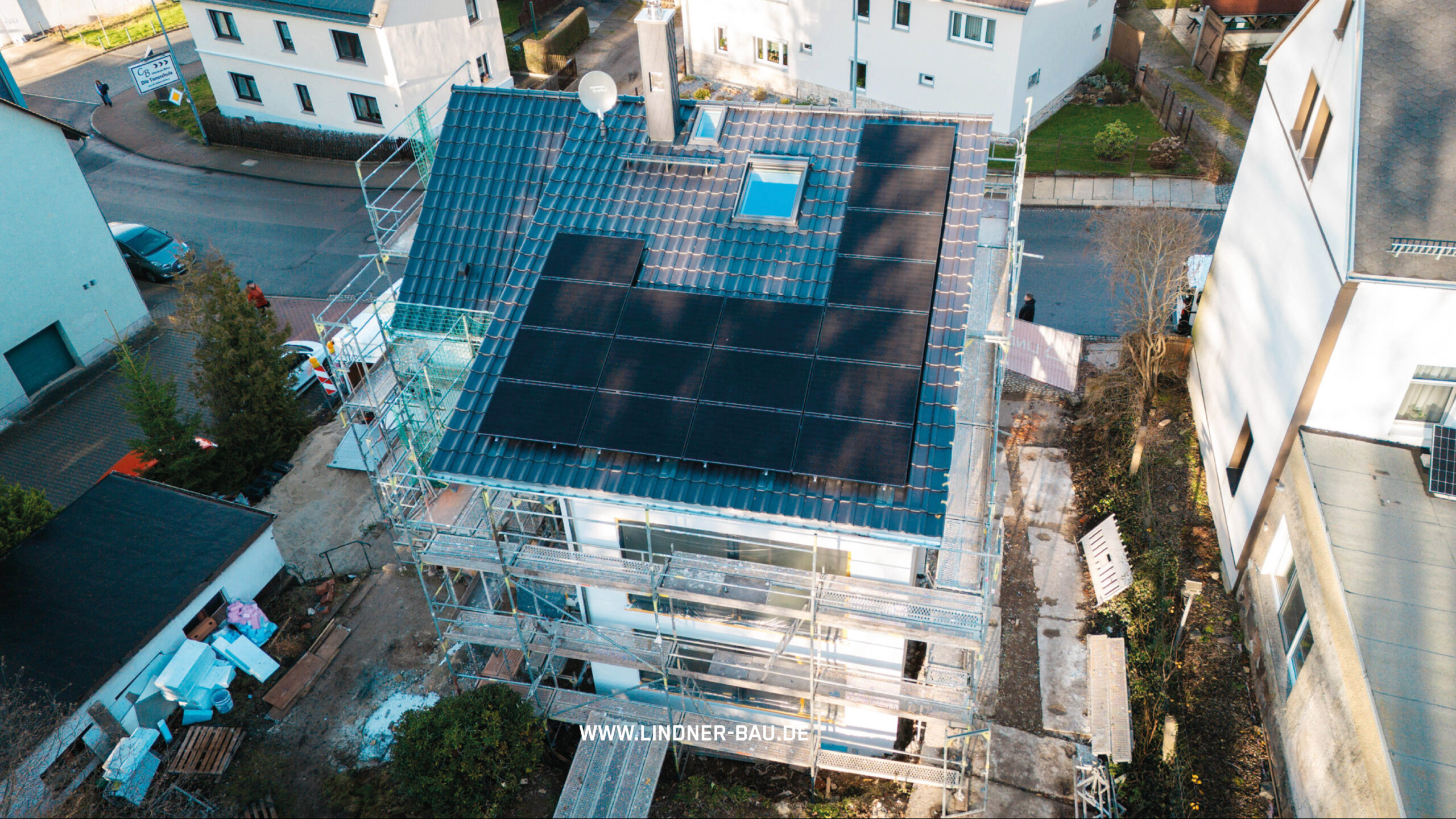 Luftaufnahme eines Einfamilienhauses mit neu gedecktem Dach und installierter Photovoltaik-Anlage von Lindner Bau.