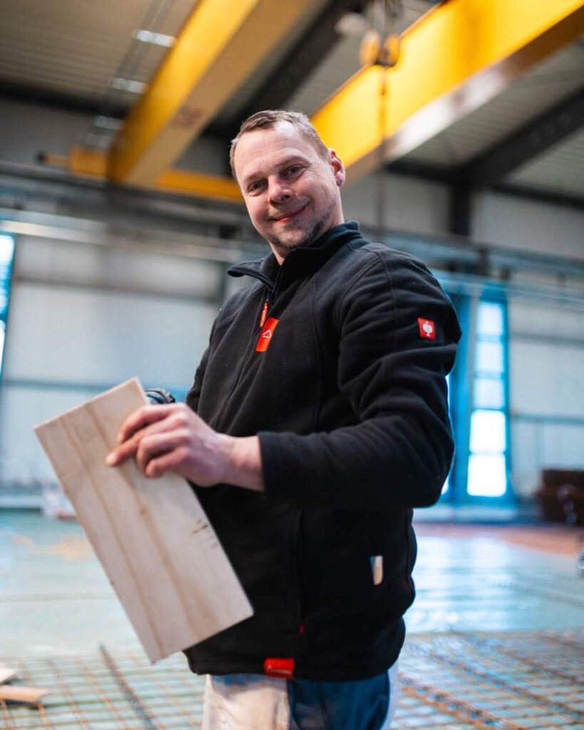 Lächelnder Mitarbeiter der Baufirma Lindner Bau hält ein Schalungselement während der Vorbereitungen auf der Baustelle in Chemnitz.