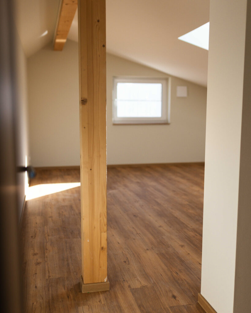Ausgebautes Dachgeschoss mit sichtbaren Holzbalken, Dachfenster und hellem Laminatboden.