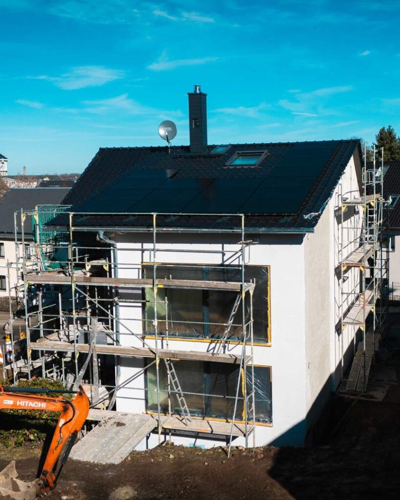 Neubau eines Einfamilienhauses mit Photovoltaikanlage auf dem Dach und Gerüst für Fassadenarbeiten während der Bauphase.

