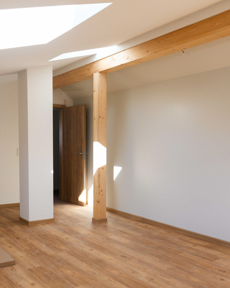 Innenarchitektur im Dachgeschoss mit Fokus auf stützende Echtholzbalken und natürlichem Lichteinfall durch Dachschrägenfenster.