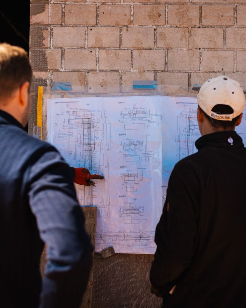Zwei Fachleute diskutieren Baupläne, die an einer Wand der Fugel-Baustelle befestigt sind.