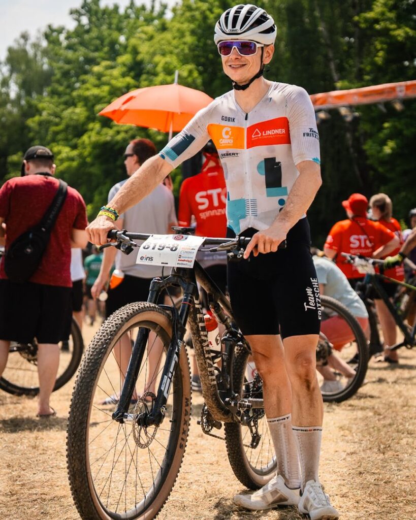 Ein sichtlich erschöpfter aber glücklicher MTB-Fahrer steht mit seinem Mountainbike im Zielbereich des Heavy24 Events