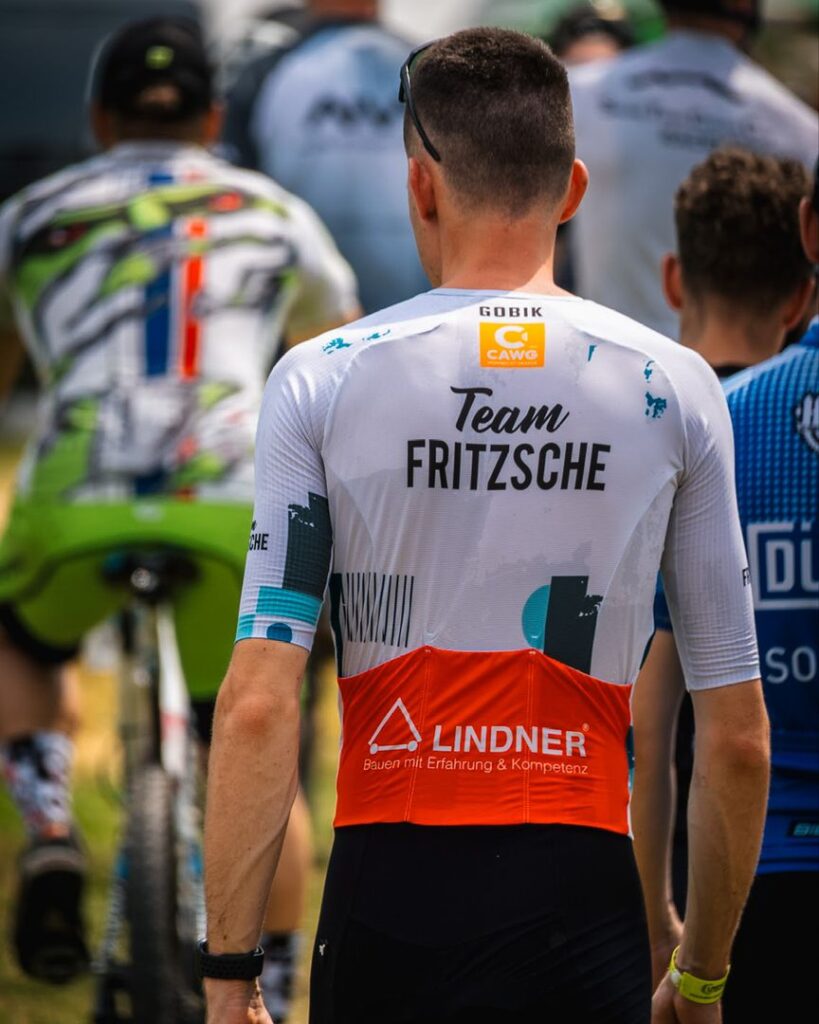 Rückansicht eines Radrennfahrers im weißen Radtrikot mit den Sponsorenlogos von Team Fritzsche und Lindner Bau
