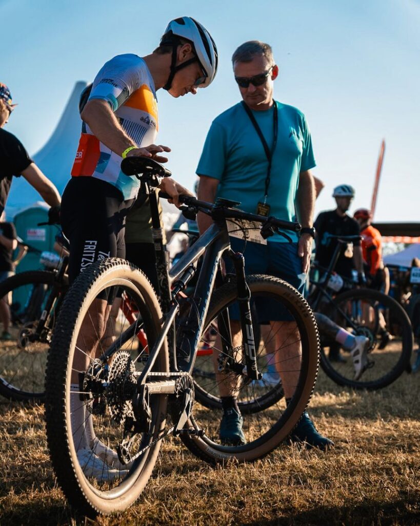Ein Radrennfahrer prüft zusammen mit einem Betreuer sein Mountainbike vor dem Start des Heavy24 Rennens