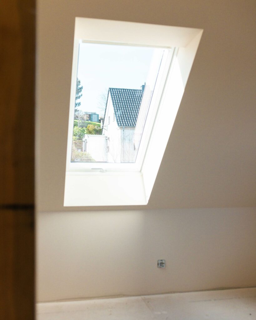 Blick durch ein modernes weißes Dachfenster im ausgebauten Dachgeschoss auf ein Nachbarhaus.