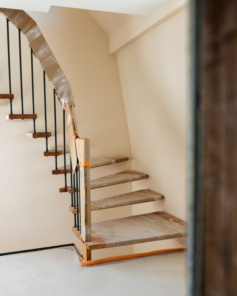 Offene Holztreppe mit schwarzen Metallstreben und Schutzfolie während der Bauphase im Einfamilienhaus.