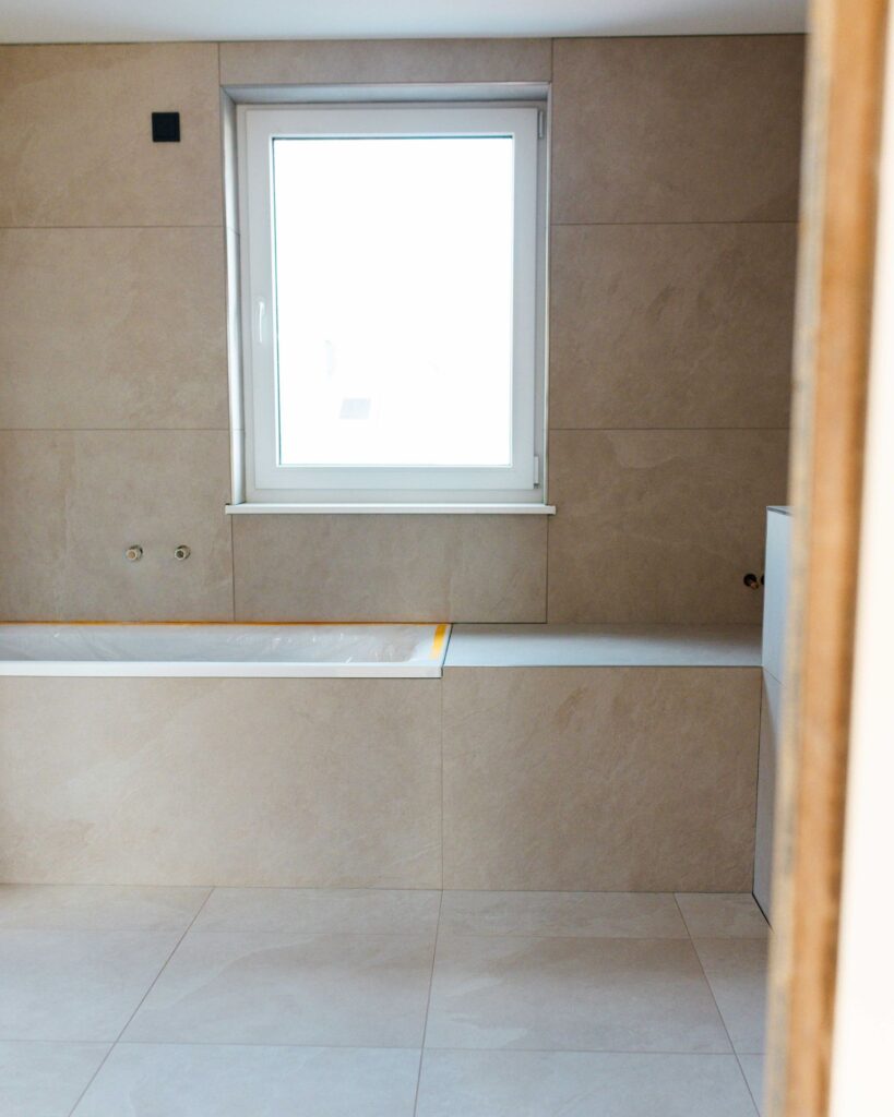 Modern gefliestes Badezimmer im Innenausbau mit eingebauter Badewanne und großem Fenster.