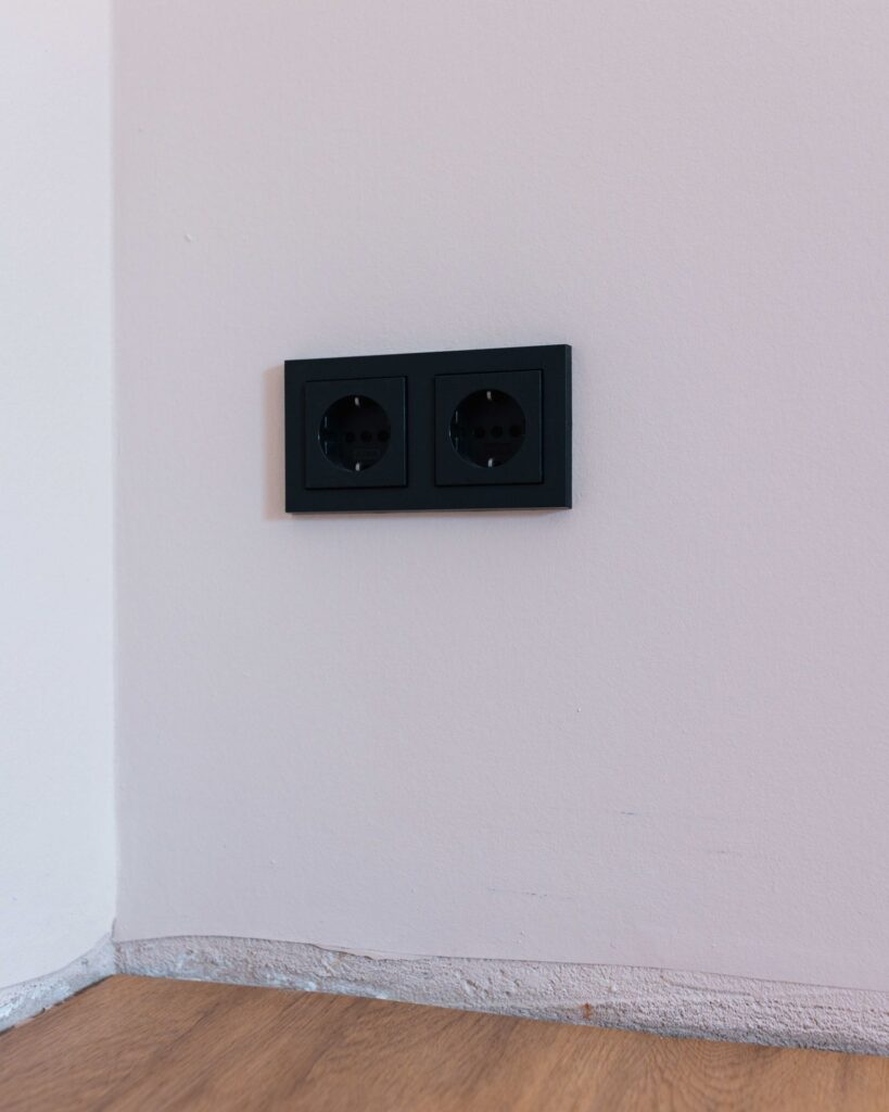 Moderne mattschwarze Doppelsteckdose an einer weiß verputzten Wand über einem Parkettboden im Neubau.
