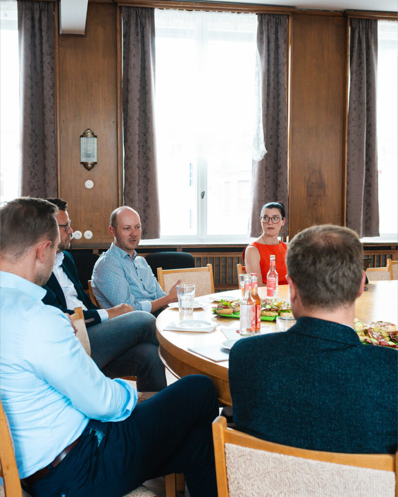 Politischer Austausch auf Augenhöhe: Große Gesprächsrunde an einem runden Holztisch mit Snacks und Getränken. Die Landtagsabgeordnete Ina Klemm hört aufmerksam zu, während die Beteiligten, darunter Alexander Dierks und Tony Lindner, im Dialog zusammensitzen.