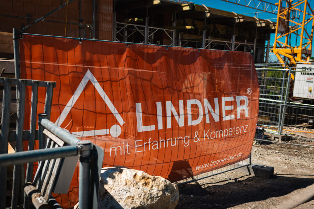 Rotes Bauzaunbanner der Firma Lindner Bau auf einer Baustelle in Chemnitz-Adelsberg vor dem Rohbau