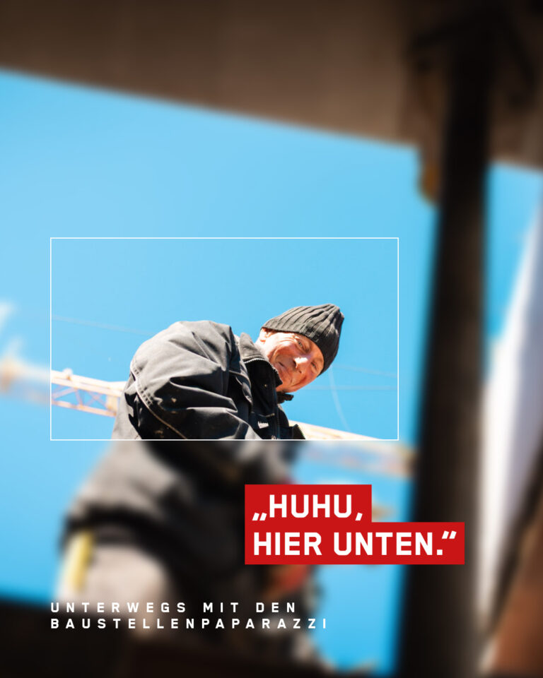 Bauarbeiter mit Mütze schaut von oben herab mit Kränen im Hintergrund, Text: Unterwegs mit den Baustellenpaparazzi – Huhu, hier unten.