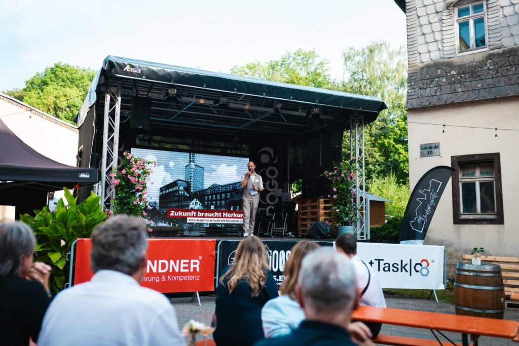 Freiluft-Vortrag auf der Festbühne im Innenhof vor sitzendem Publikum.