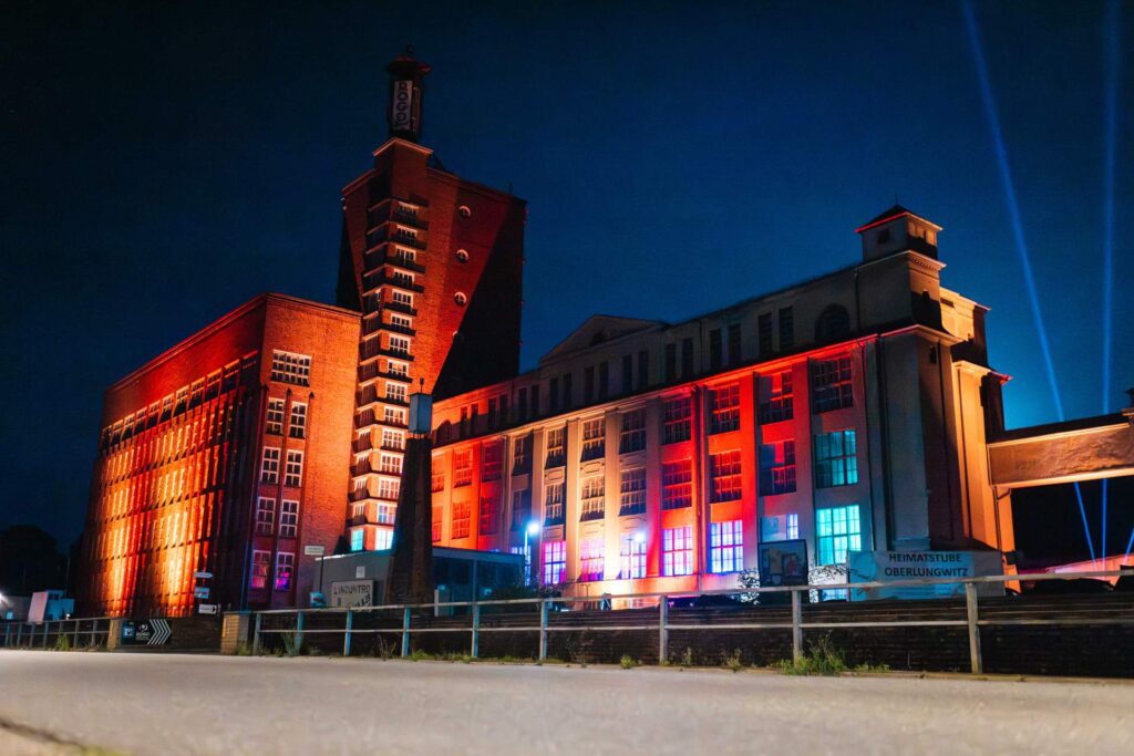 Bunt beleuchtete Fassade der ehemaligen ROGO-Werke in Oberlungwitz bei Nacht.
