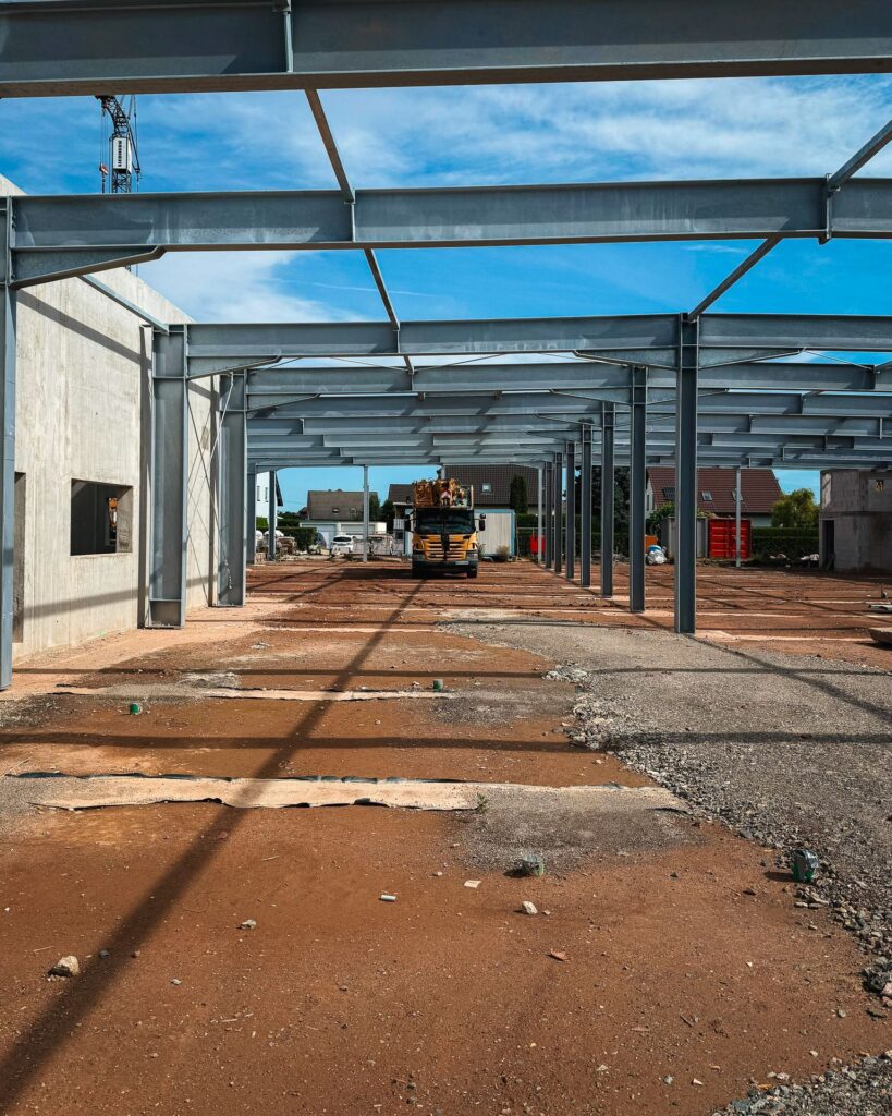 Längsansicht Hallenrohbau: Blick durch die gesamte Länge des Stahltragwerks einer Industriehalle auf den Erdboden und einen gelben LKW in der Ferne.