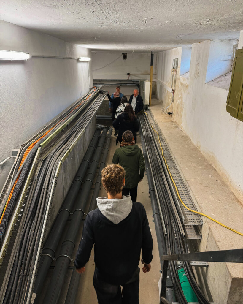 Teilnehmer gehen durch einen Versorgungsgang mit Kabeltrassen während der ROGO-Werk Besichtigung
