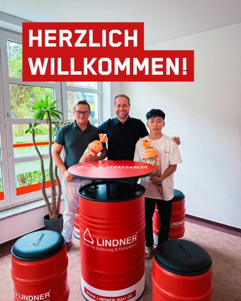 Tony Lindner steht mit zwei neuen Azubis vor roten Stehtischen. Die Azubis halten Zuckertüten in der Hand